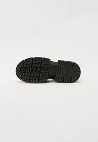 Crna gumena potplata cipele s teksturiranim uzorkom. Sadrži utisnute riječi "BUFFALO" i detalj u obliku okruglog loga.