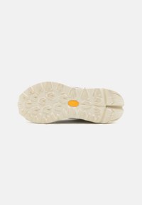 Light rubber outsole with deep, aggressive tread pattern; beige color; includes a yellow logo detail at the center for traction and durability.