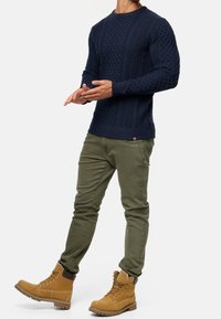 Navy blue knitted sweater with textured patterns, paired with olive green tapered pants and tan lace-up boots.