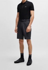 Svart polo med vit krage och logo, matchad med mörka shorts, svart bälte, svarta strumpor och svarta sneakers.