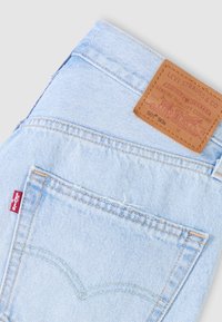 Svijetloplave jeans hlače od trapera s kožnom oznakom na stražnjoj strani, ukrašene narančastim šavovima i crvenom Levi's oznakom na bočnom džepu.