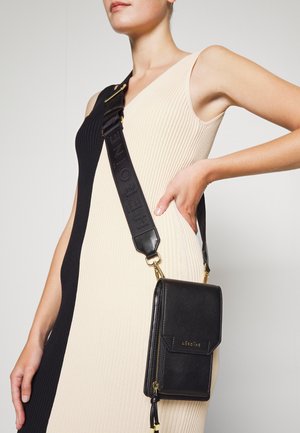 Czarna skórzana torebka na ramię z fakturowaną powierzchnią, złotymi okuciami i szerokim tłoczonym paskiem. Torebka posiada zamek błyskawiczny i przednią klapę.