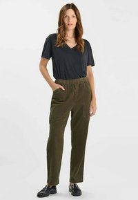 T-shirt noir à col en V associé à un pantalon en velours côtelé vert olive avec une ceinture élastique et des poches latérales, porté avec des chaussures noires.