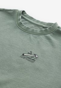 Sudadera verde con un cuello acanalado que presenta un gráfico negro de un martillo y el texto "REPARACIONES DE MANITAS" en negrita. Textura suave de algodón.