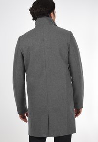 Abrigo de lana gris con cuello alto, textura suave, ajuste entallado y detalles de costura vertical, vista desde la parte trasera.