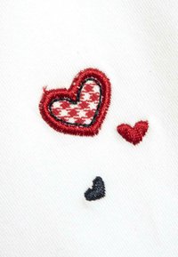 Cuori ricamati rossi e neri su tessuto bianco; il cuore più grande presenta un motivo a scacchi; texture liscia con contorni in contrasto.