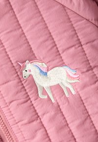 Unicorno bianco ricamato con criniera e coda in tonalità pastel rosa, blu e gialla su uno sfondo in tessuto rosa trapuntato.