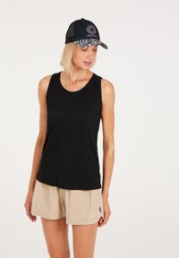 Top nero senza maniche in tessuto testurizzato, abbinato a pantaloni corti beige. Il cappellino presenta un bordo floreale e un logo centrale rosa su sfondo navy.