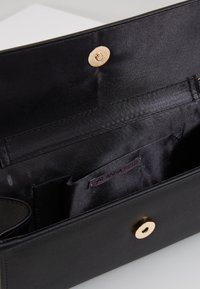 Černý syntetický interiér tašky s hladkou texturou, s ozdobným zlatým uzávěrem a vnitřní etiketou "ANNA FIELD."