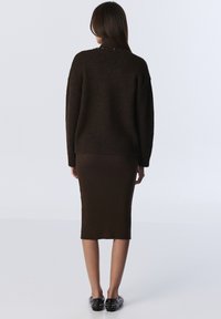 Bordeaux gebreide trui met een losse pasvorm, geribde zoom en decoratieve accenten bij de kraag; gecombineerd met een aansluitende bordeaux geribde midi-rok.