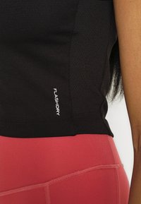 Black moisture-wicking athletic top with mesh texture, featuring the "FLASHDRY" logo in white. Paired with pink fitted leggings.