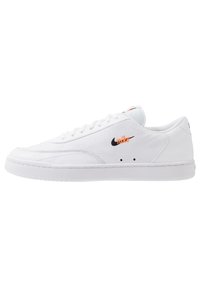 Sneaker alb din piele cu un finisaj texturat, logo negru și accent portocaliu. Prezintă șireturi albe și o talpă din cauciuc.