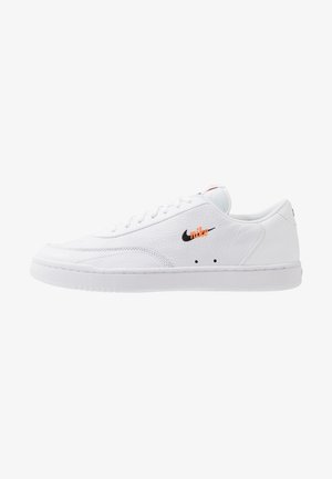 Biele kožené tenisky s textúrovaným povrchom, čiernym logom a oranžovým akcentom. Disponujú bielymi šnúrkami a gumovou podrážkou.