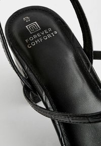 Černé sandály z umělé kůže s nastavitelnými popruhy, texturovanou stélkou a stříbrným logem "Forever Comfort" na vnitřní straně. Akcenty v kroko vzoru.