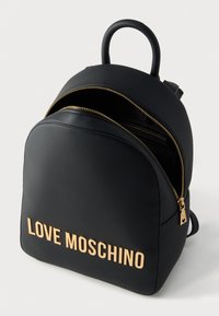 Μαύρο σακίδιο πλάτης από συνθετικό δέρμα με στρογγυλεμένο σχήμα, διακοσμημένο με έντονο χρυσό λογότυπο "LOVE MOSCHINO" και χρυσές λεπτομέρειες στο φερμουάρ.