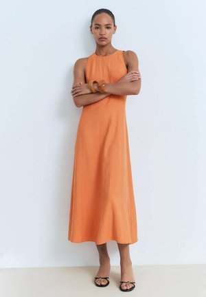 Robe longue sans manches orange en tissu léger, avec un col rond. Accessoirisée avec un bracelet épais et des sandales noires.