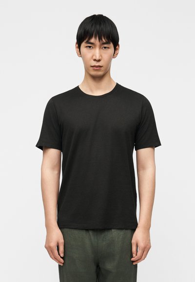 T-shirt noir à col rond en tissu doux ; manches courtes ; coupe décontractée ; porté avec un pantalon vert olive ; design minimaliste.
