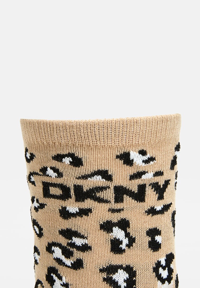 Beige gebreide sokken met een zwart-wit luipaardenprint en de tekst "DKNY" prominent weergegeven. Zachte textuur, met een opgerolde rand.