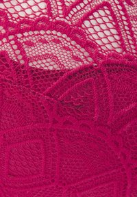 Sarkans mežģīņu audums ar sarežģītām ziedu un ģeometriskām zīmēm, demonstrējot smalku acu un izsmeļošu izšuvumu tekstūru.