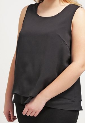 Sleeveless black layered blouse worn by a person, showing upper torso and arms against a plain background.