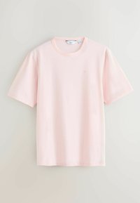T-shirt rose pâle à manches courtes et col rond, taille moyenne avec un logo discret sur le côté gauche de la poitrine, présenté sur un fond clair uni.