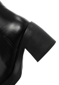 Stivale alla caviglia in pelle nera con tacco a blocco di altezza media. Presenta una texture liscia e dettagli sul tacco rigati per una migliore aderenza.