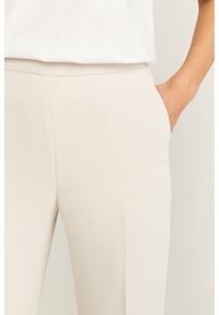 Beiga skräddarsydda byxor med en slät yta, sidofickor och en åtsittande midja, kombinerat med en vit topp.