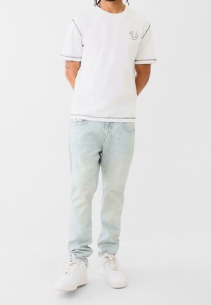 White cotton t-shirt with short sleeves and gray stitching, featuring a small logo. Light blue denim jeans with a faded texture and slim fit.