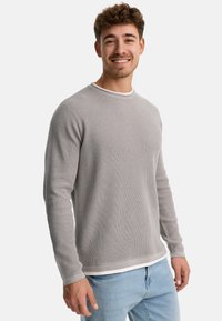 Suéter gris de manga larga con punto texturizado, ribete blanco en el escote y el dobladillo. Combinado con jeans de un azul claro.