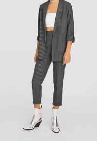 Blazer gris à fines rayures et pantalon assorti aux manches retroussées, associé à un crop top blanc. Bottines argentées métalliques à talons blocs.