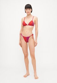 Bikini set s gradijentnim dizajnom u crvenoj i ljubičastoj boji, s trokutastim gornjim dijelom i vezanim donjim dijelom sa strane, izrađen od glatkog materijala sa naboranim rubovima.