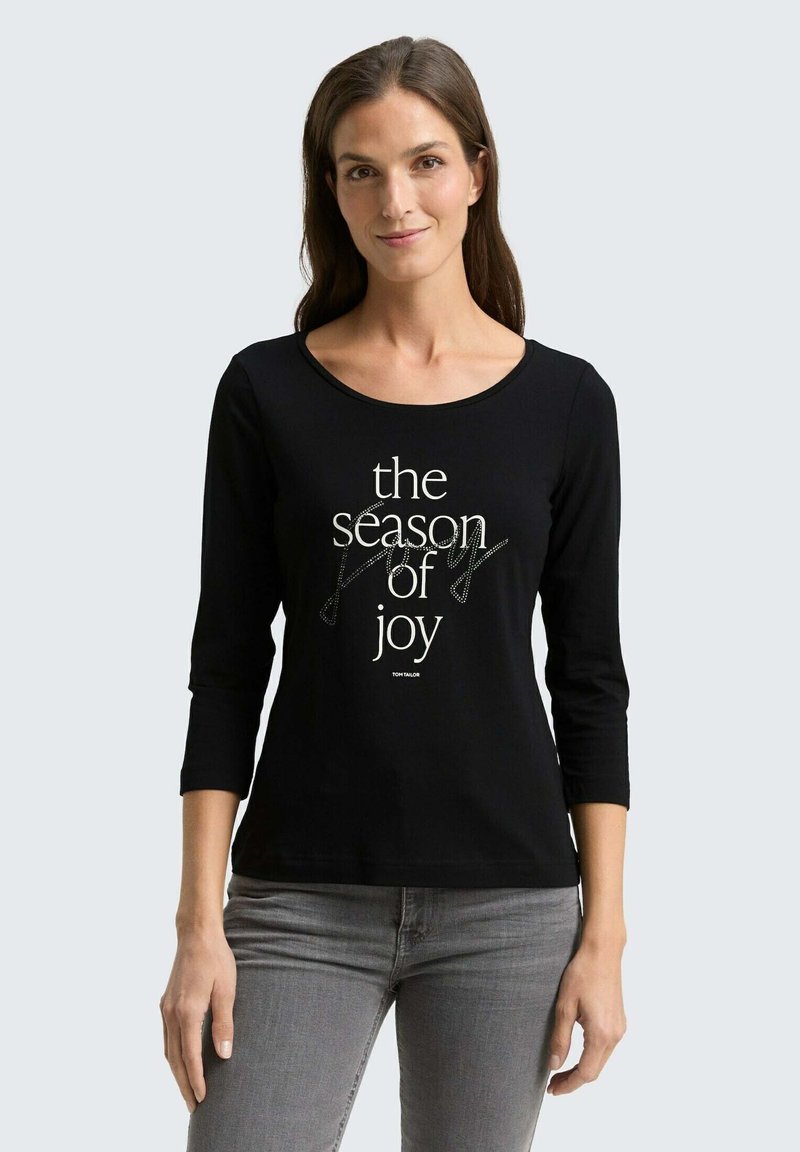 Zwarte lange mouwen t-shirt met een ronde hals, voorzien van witte tekst "het seizoen van vreugde" in verschillende lettergroottes en stijlen. Soepele katoen stof.