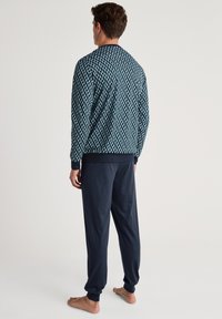 Marineblauwe lange mouwen jack met geometrisch patroon, gecombineerd met effen marineblauwe broek. Zachte textuur, elastische manchetten bij de polsen en enkels.