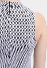 Sukienka bez rękawów z ustrukturyzowanym dekoltem, charakteryzująca się teksturowanym czarno-białym wzorem geometrycznym i zamkiem błyskawicznym z tyłu.