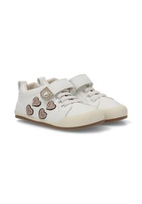 Zapatillas blancas para niños con suelas beige, parches brillantes en forma de corazón a los lados, cordones y una correa de velcro con un ícono de pie.