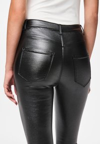 Μαύροι κολάν από συνθετικό δέρμα με γυαλιστερή υφή, με πίσω τσέπες και ραμμένες λεπτομέρειες. Λεία, εφαρμοστή σχεδίαση.