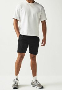 T-shirt en coton blanc à manches courtes, associé à un short noir. Chaussures de sport grises avec semelles blanches et chaussettes à côtes au niveau de la cheville.