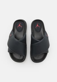 Sandales slide noires rembourrées avec des sangles croisées et des logos Jumpman rouges sur les semelles et les sangles extérieures, vues de dessus sur fond blanc.