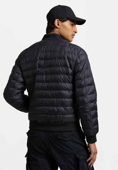 Svart puffjakke med quiltet design og ribbede mansjetter. Har høy krage og er parret med mørke cargo-bukser. Vist fra baksiden.