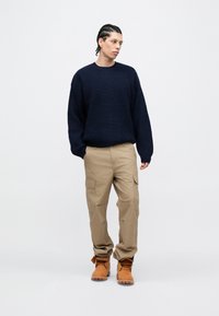 Maglione lavorato a maglia blu navy, pantaloni cargo beige e stivali color cuoio. Il maglione presenta un motivo a rilievo, mentre i pantaloni hanno tasche laterali e una vestibilità dritta.