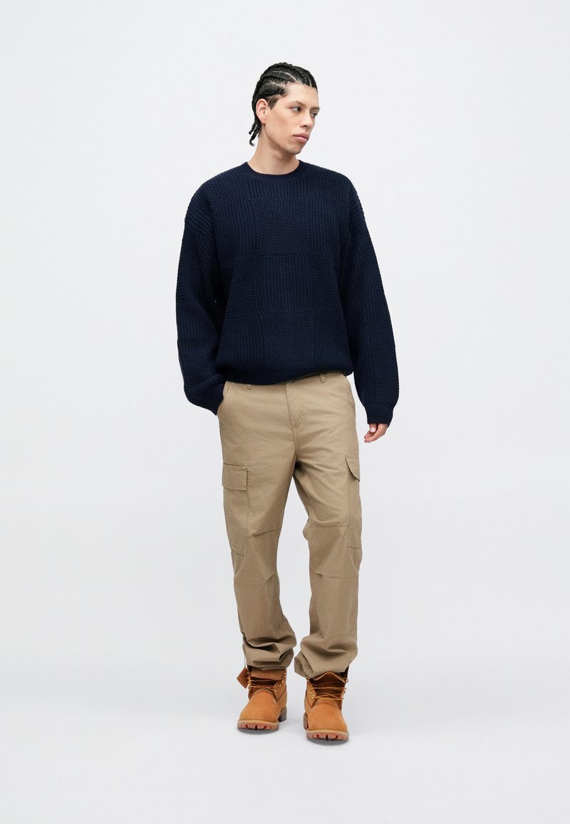 Navy knitted sweater, beige cargo pants, and tan boots. The sweater features a textured design, while pants have side pockets and a straight fit.
