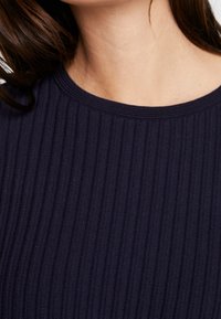 Laivastonsininen ribbineulepaita pyöreällä pääntiellä, jossa pystysuora tekstuuri ja vartalonmyötäinen istuvuus tiukkaa istuvuutta varten.