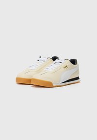 Sneakers made from cream synthetic material with white accents, black heel, and gum rubber outsole; features white laces and logo detail.