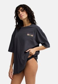 Σκούρο γκρι φαρδιά μπλούζα από βαμβάκι με λουλουδένιο λογότυπο τυπωμένο στο στήθος. Κοντά μανίκια και άνετη εφαρμογή.