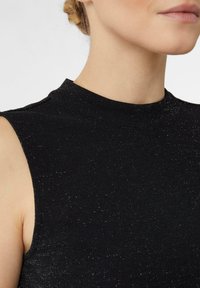 Zbliżenie na szyję i ramię kobiety, która ma na sobie bezrękawnik z czarnym brokatem o wysokim dekolcie, włosy związane do tyłu.