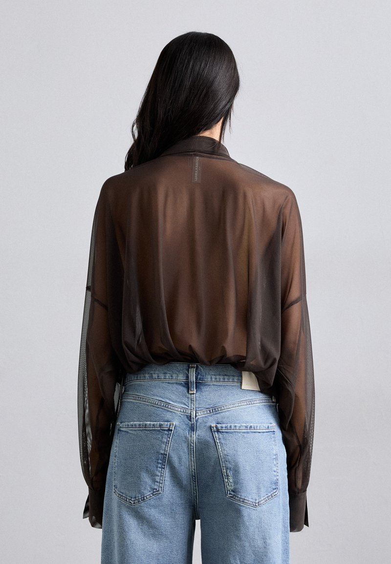 Blusa trasparente marrone con maniche lunghe e colletto, abbinata a jeans di denim blu a vita alta con tasche posteriori e un'etichetta interna.