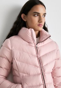 Φωτεινό ροζ φουσκωτό μπουφάν με ψηλό γιακά και οριζόντια ραφή. Διαθέτει κλείσιμο με φερμουάρ και ασημένια διακοσμητικά στοιχεία.