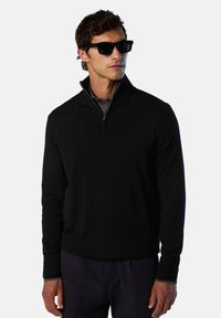 Maglione pullover con zip nera, maniche lunghe, texture liscia e colletto interno a contrasto. Indossato con occhiali da sole scuri.
