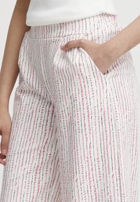Pantalons larges en tissu léger, arborant des rayures verticales roses, noires et bleu clair, avec une poche latérale et une taille élastique.