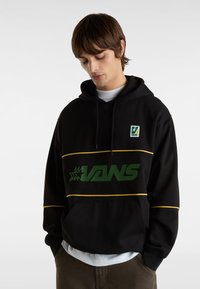 Svart huvtröja med grön "VANS"-logga, gula stripes detaljer och en framficka. Har ett mysigt tyg och justerbar dragsko på huven.